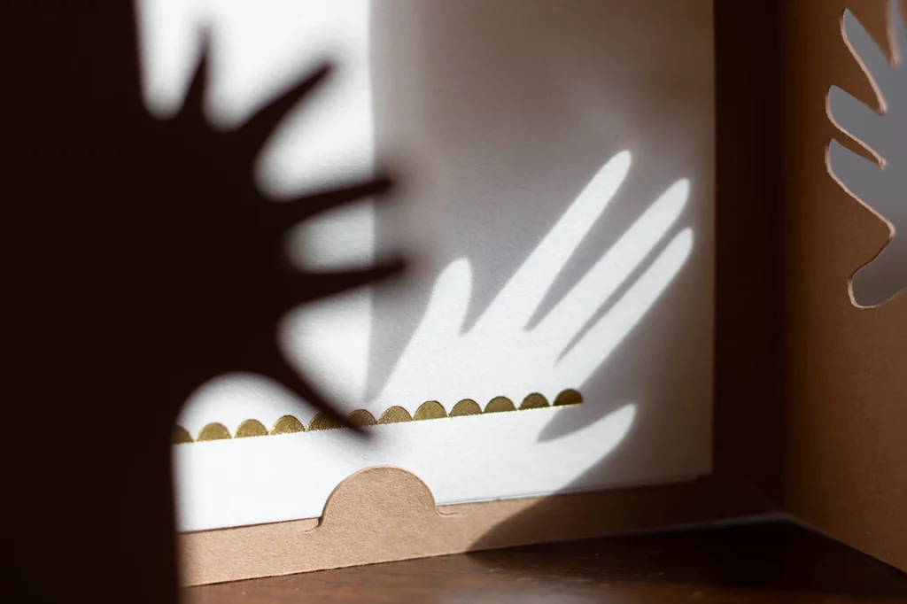 Photo du bas du livret de cartes empreintes pour bébé personnalisable ouvert, avec un effet d'ombrage de la main, couleur cocos, et des ornements faits à la dorure à chaud.