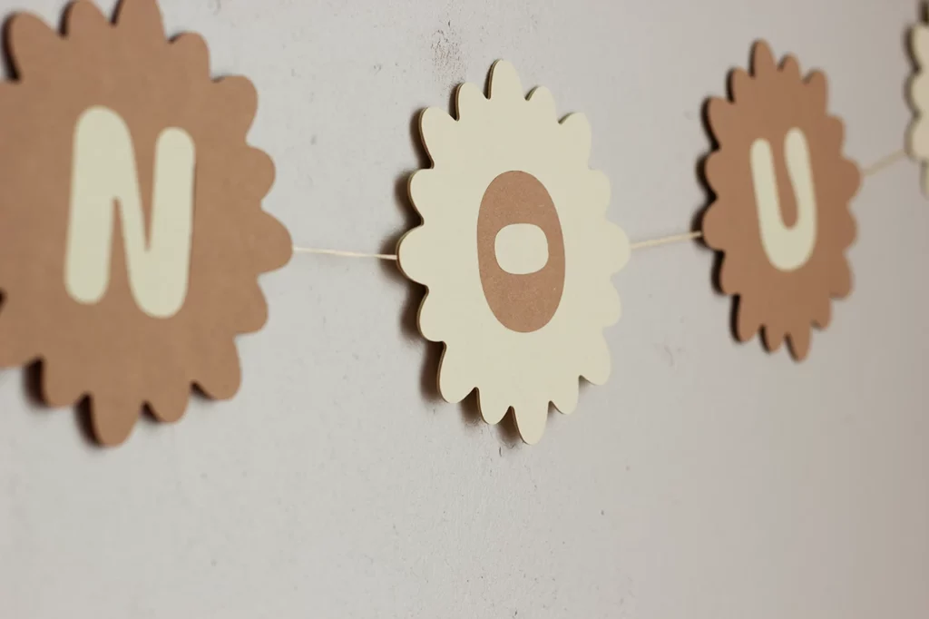 Zoom sur la guirlande prénom en marqueterie de papier personnalisable, avec le prénom Anouk, couleur vanille et cocos.