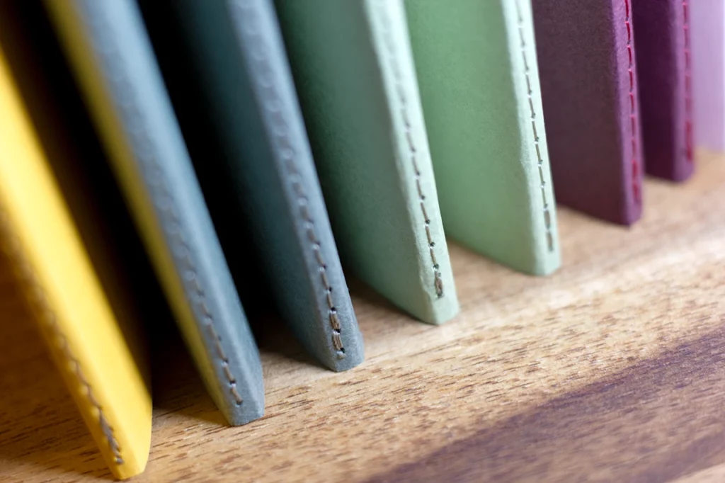 Zoom sur le bas des carnets faits main à l'atelier Forme contre forme avec une reliure Singer et des couvertures colorées en vues de dos.