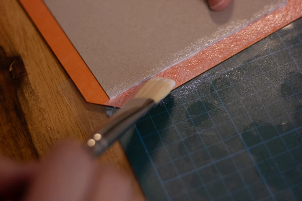 Application de colle au pinceau pour le rembordage de la couverture en cuir de pomme orange.