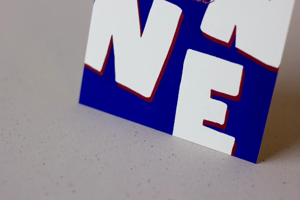 Zoom sur le bas de la carte « Bonne Année », imprimée en letterpress bleu et rouge.