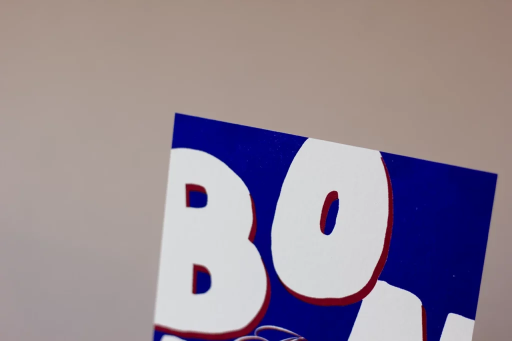 Zoom sur le haut de la carte « Bonne Année », imprimée en letterpress bleu et rouge.