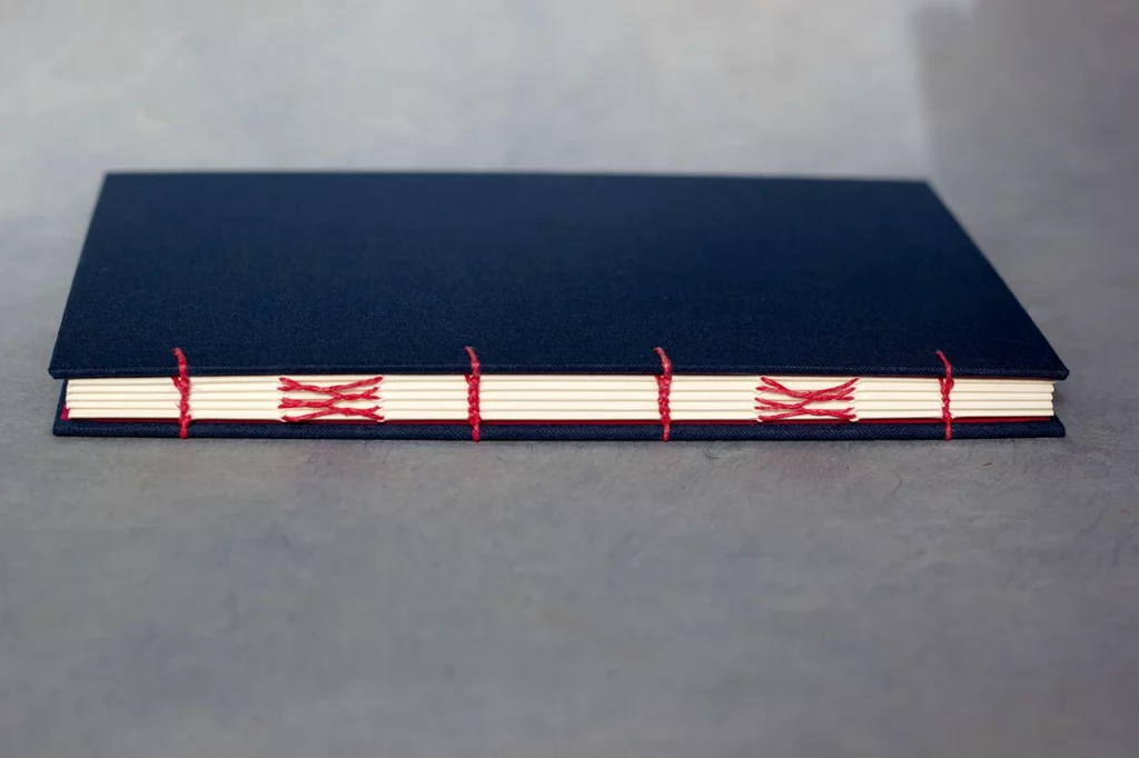 Carnet sur mesure en reliure copte, couverture en toile du Marais bleu marine et couture au fil de lin rose fuchsia — Atelier Forme contre forme, Bordeaux.