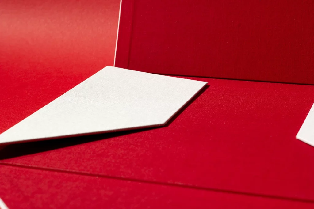 Portefeuille à quatre rabats ouvert avec un rabat refermé, réalisé en toile de reliure du Marais Nude et rouge — Atelier Forme contre forme, Bordeaux.